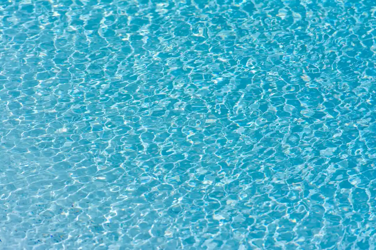 Piscine extérieure à l'eau claire et turquoise, entourée d'une terrasse, par une journée ensoleillée