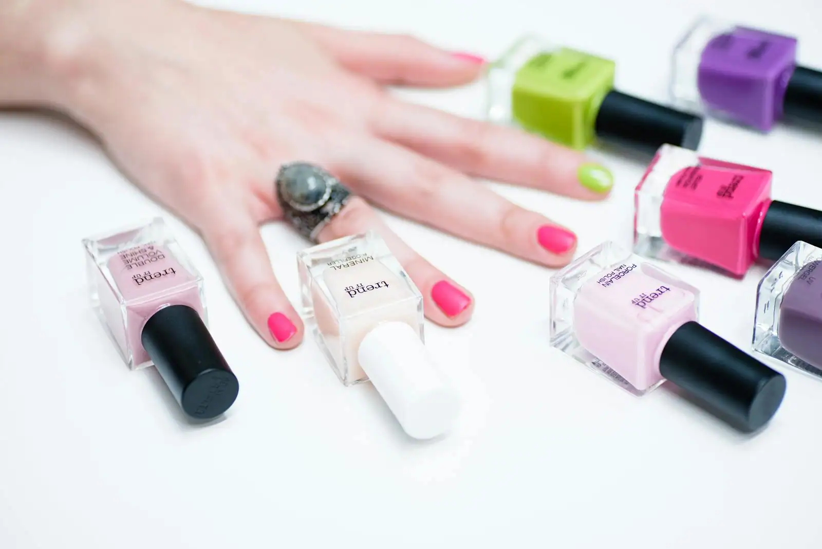 Mains aux ongles décorés de motifs colorés posées sur une table avec flacons de vernis