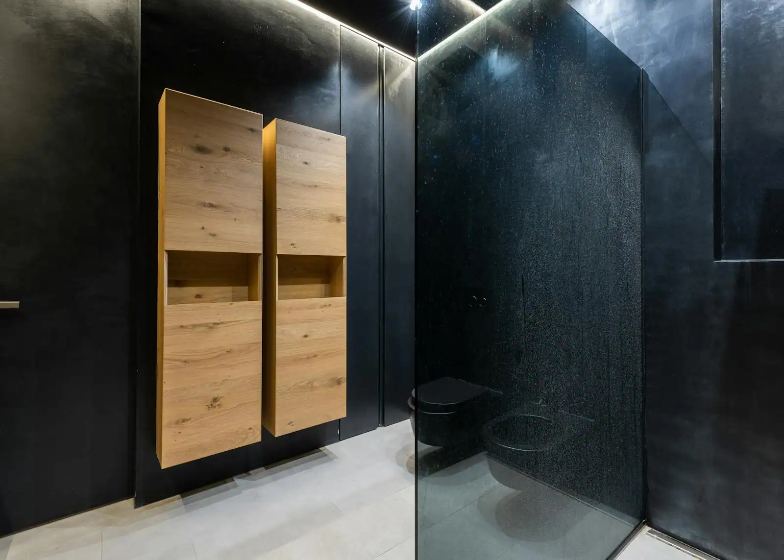 WC suspendu dans des toilettes décorées avec mur sombre, tablette et plante verte