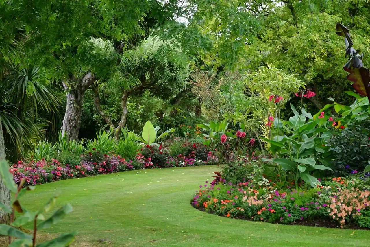 Jardin paysager structuré avec terrasse en bois, massifs fleuris et allée traversant une pelouse