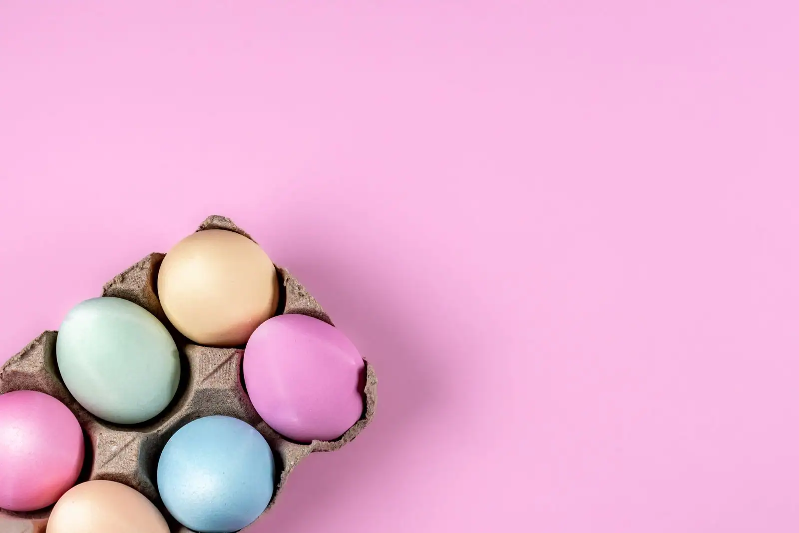 Œufs de Pâques teintés aux tons pastel disposés dans un casier à œufs sur fond rose