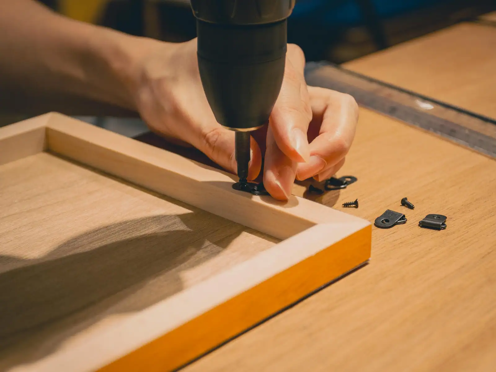 Mains fixant une patte de fixation sur un cadre en bois à l'aide d'une perceuse-visseuse