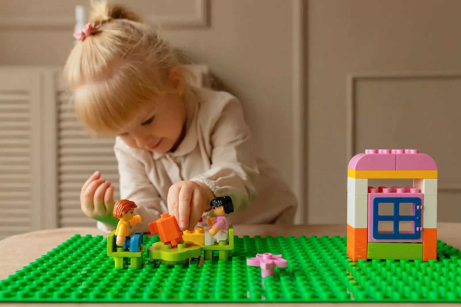 Enfant assemblant des briques de construction colorées et une maisonnette sur une plaque de base verte