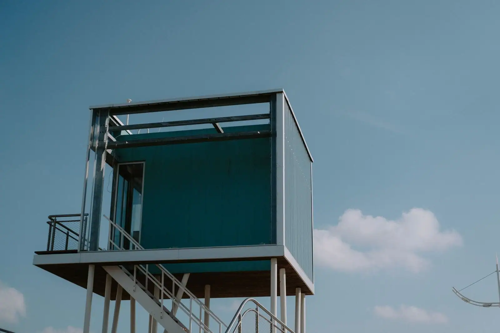 Module cubique contemporain à bardage moderne, surélevé sur pilotis avec escalier, sous un ciel bleu