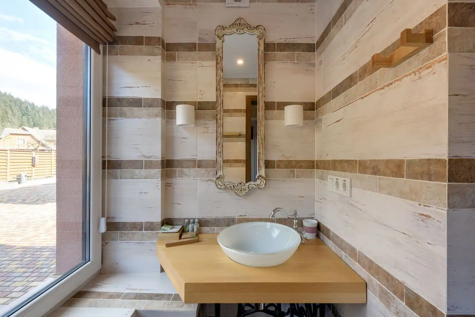 Salle de bain lumineuse aux tons beiges, avec vasque blanche sur plan en bois et miroir près d'une grande fenêtre