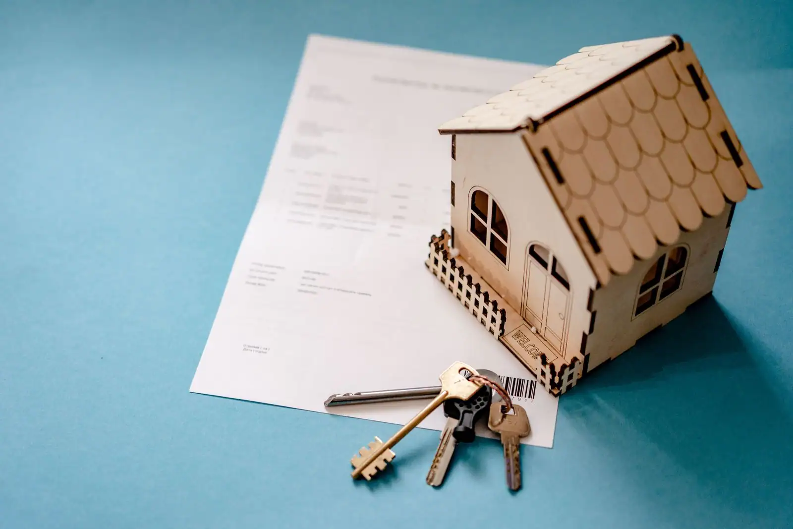 Maquette de maison en bois, trousseau de clés et document posés sur un fond bleu, illustration de l'estimation immobilière