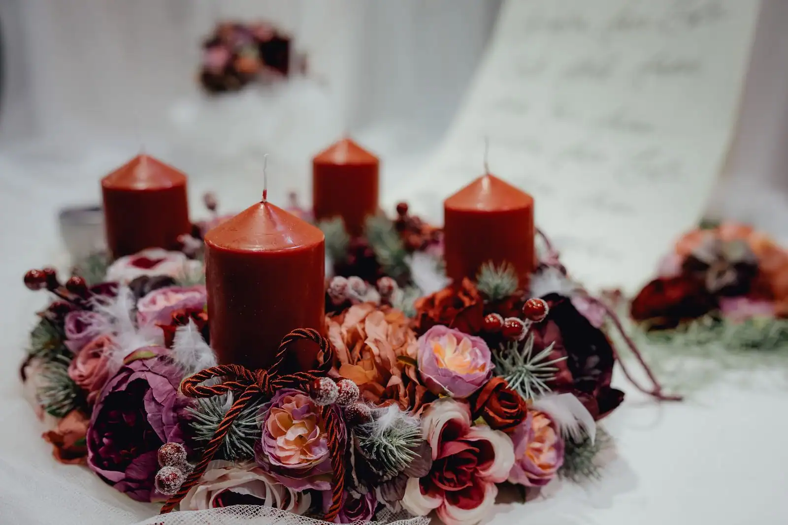 Composition de fleurs roses et mauves disposée autour de bougies sur une table claire