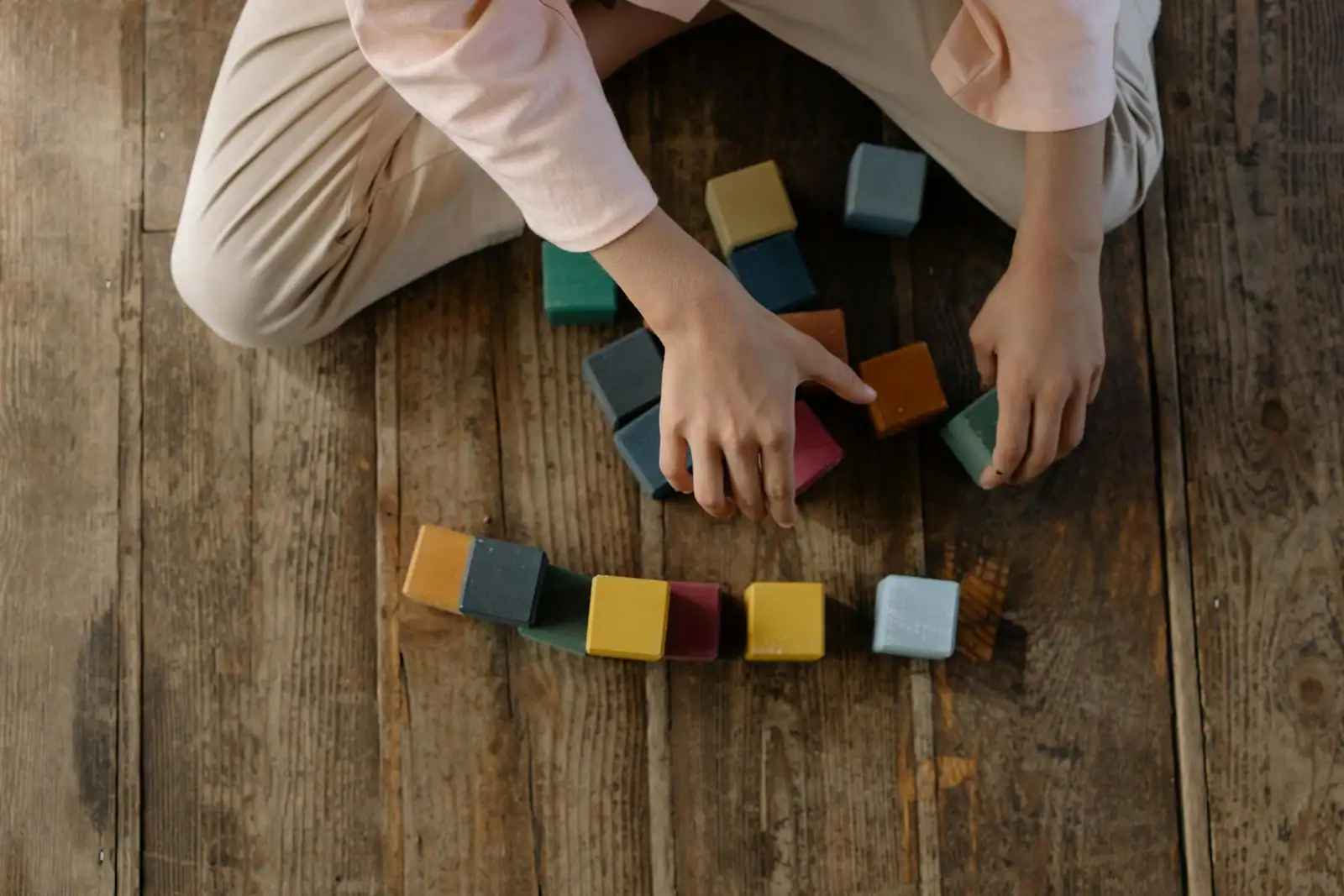 Enfant disposant des cubes de construction en bois colorés sur un parquet