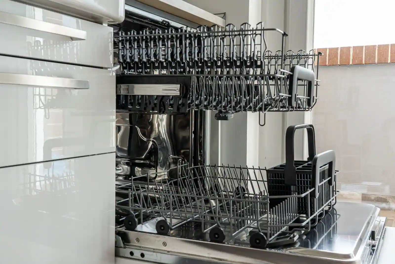 Lave-vaisselle encastrable ouvert dans une cuisine, paniers et tiroir à couverts visibles