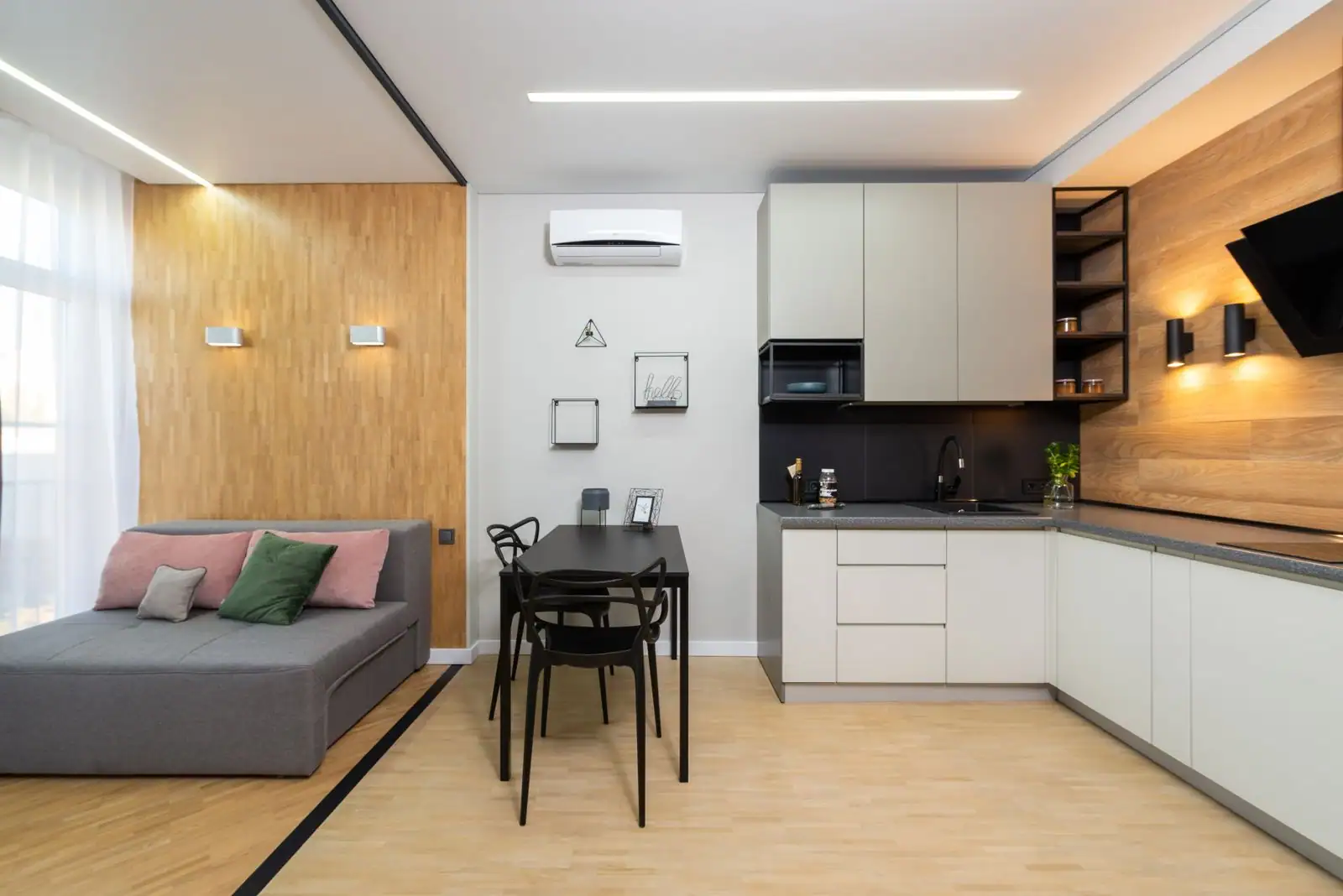 Studio moderne d'une seule pièce, avec canapé-lit gris, coin repas et kitchenette ouverte