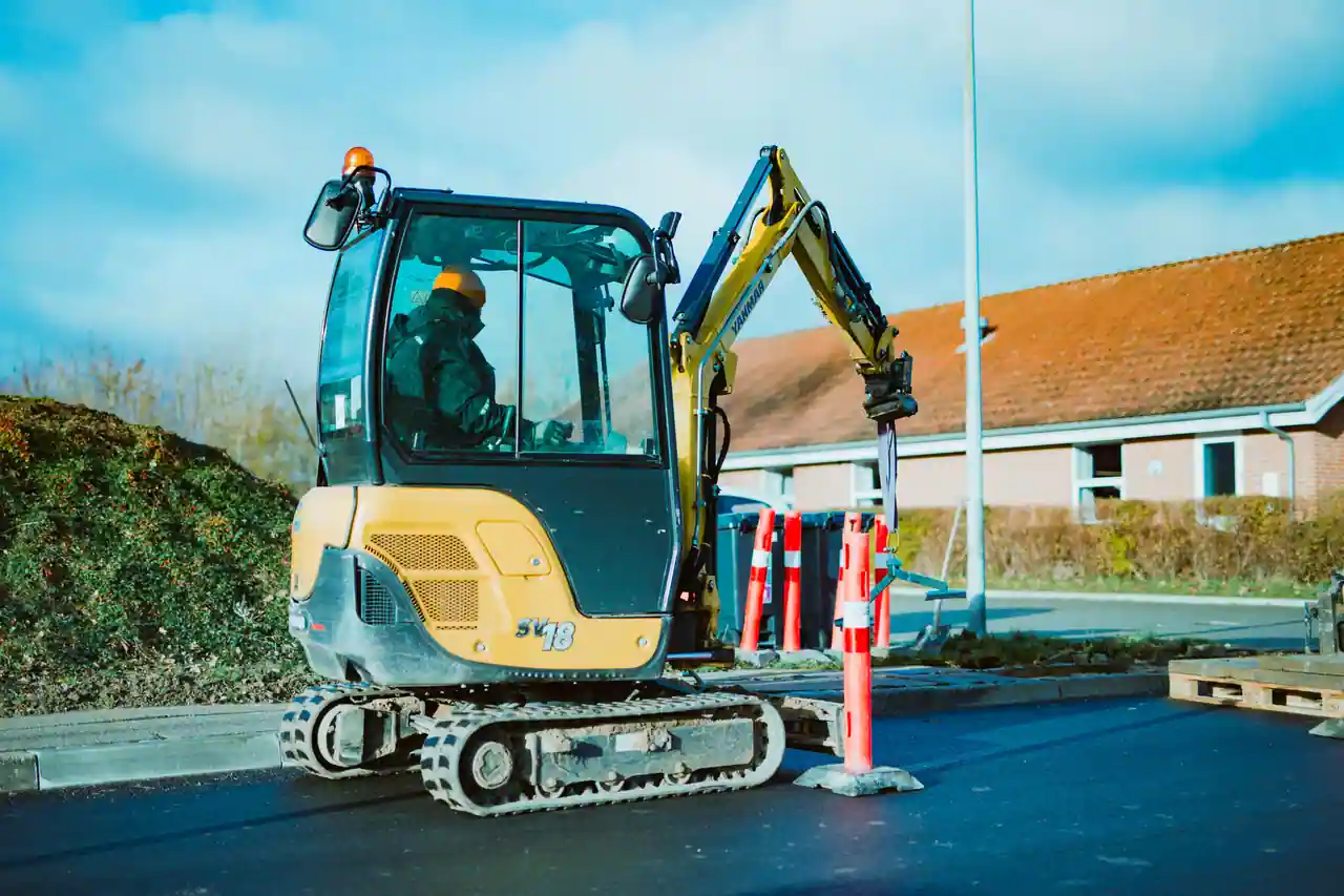 Mini-pelle compacte à chenilles avec opérateur en cabine, bras déployé sur un chantier en extérieur.