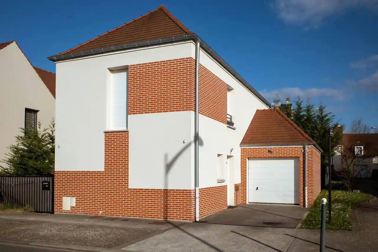 Maison individuelle à façade en briques et enduit, avec garage et allée, vue de l'extérieur.
