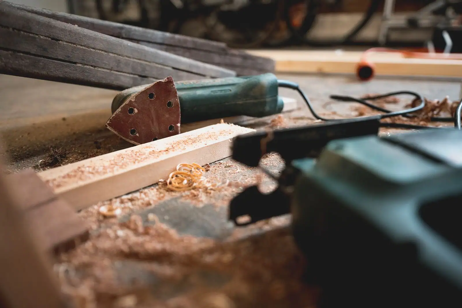 Ponceuse électrique et outils posés sur un établi en bois couvert de sciure dans un atelier, illustration de l'univers de l'outillage
