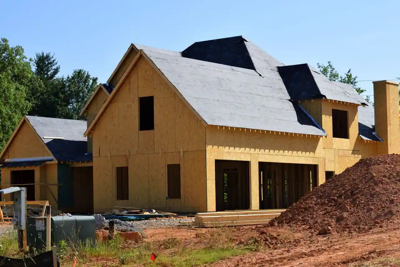 Maison individuelle en cours de construction, structure et charpente montées, sur un chantier sous un ciel dégagé