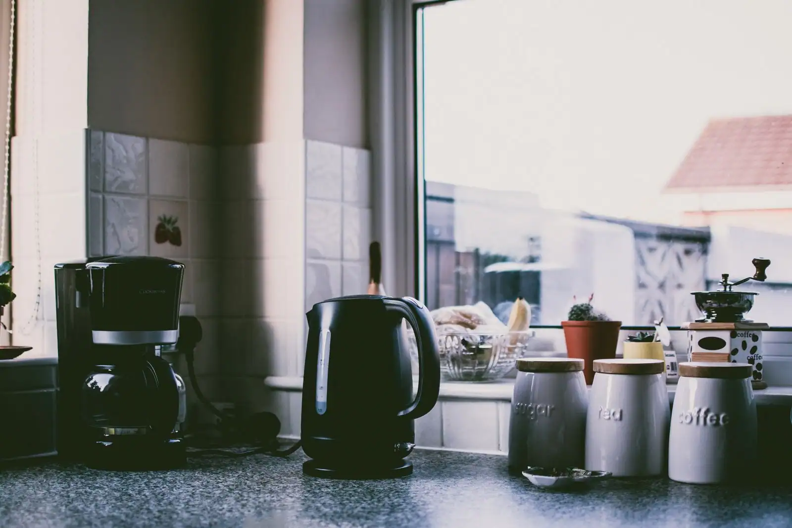 Cafetière et bouilloire électriques posées sur un plan de travail de cuisine près d'une fenêtre