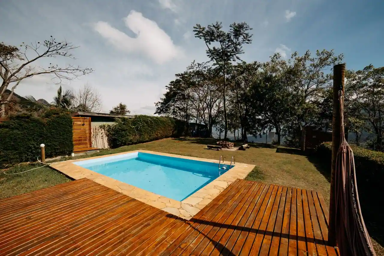Piscine extérieure bordée d'une large terrasse en bois dans un jardin verdoyant.