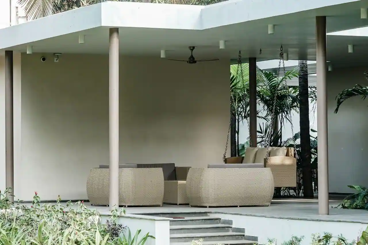 Salon de jardin en résine tressée, fauteuils et table sur une terrasse couverte entourée de verdure.
