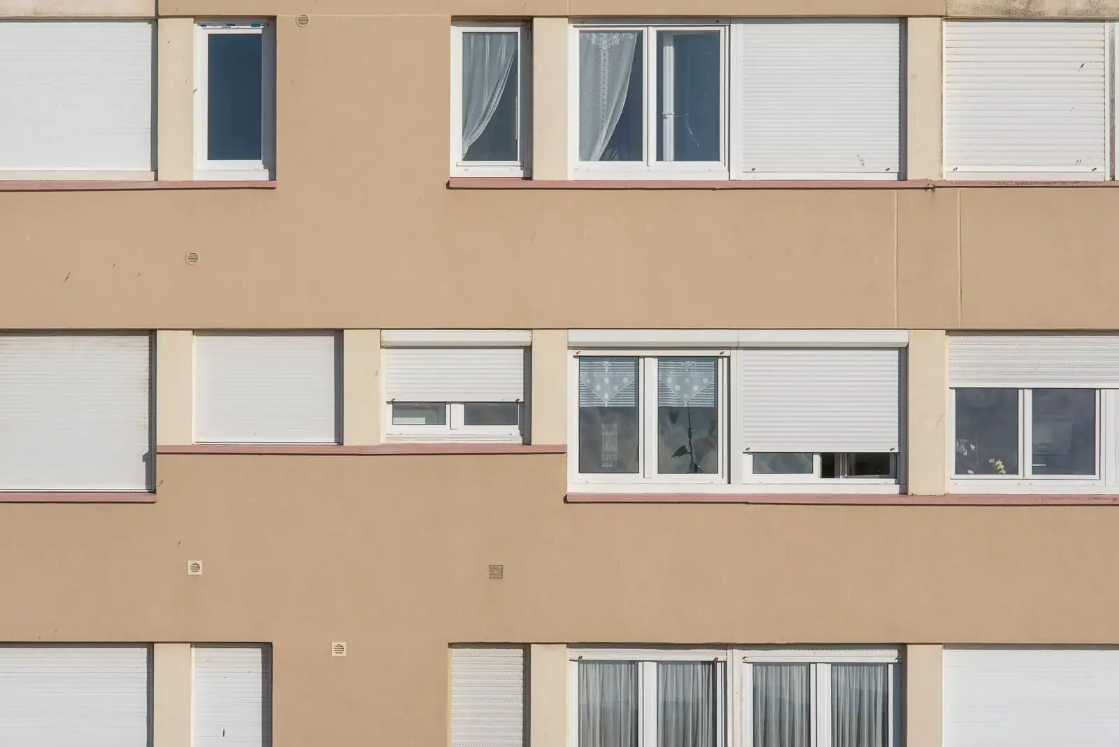 Façade d'immeuble résidentiel aux fenêtres équipées de volets roulants blancs, certains à demi baissés