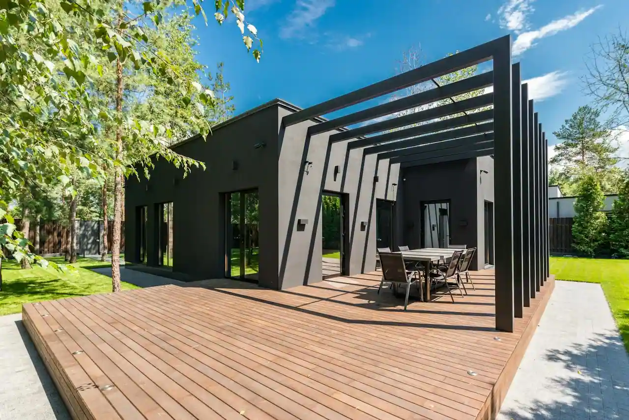 Terrasse en bois aux lames régulières devant une maison moderne, avec table et pergola dans un jardin.