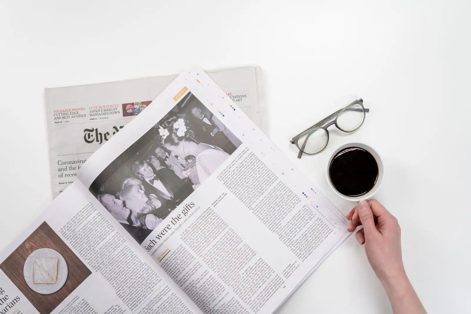 Une personne lit un journal papier plié, une tasse de café à côté, dans la lumière du matin.