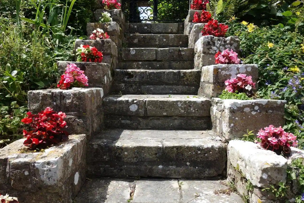 Escalier de pierre gravissant un jardin en pente, bordé de massifs fleuris de géraniums rouges et roses