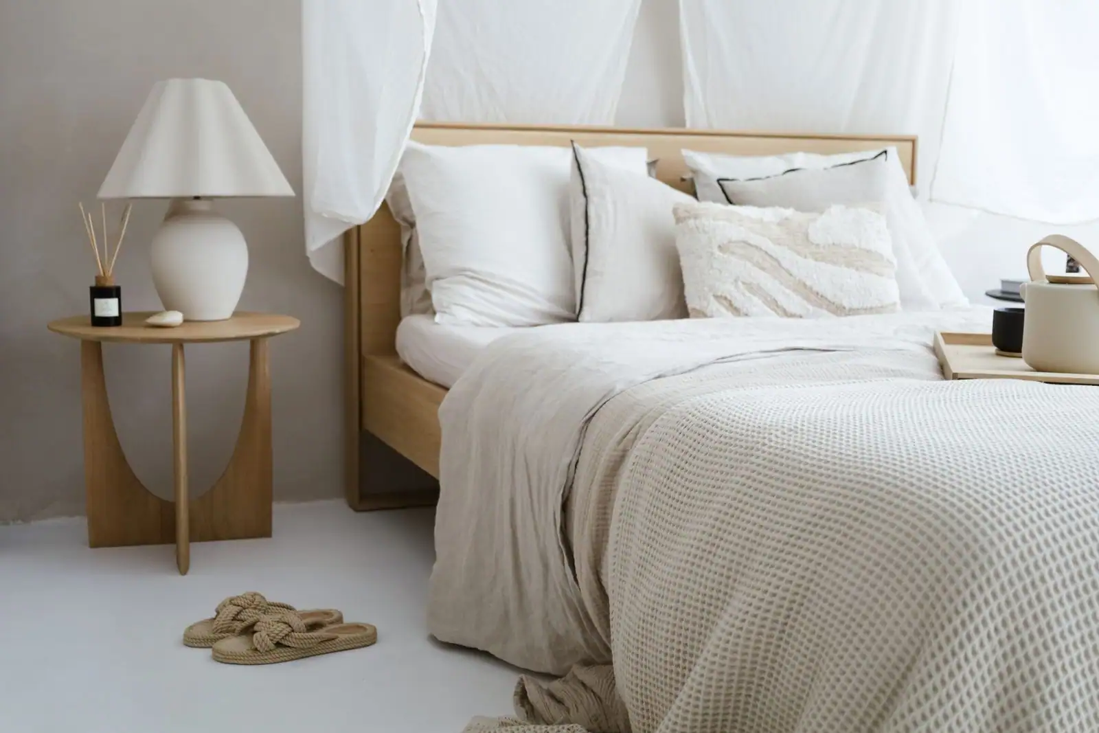 Chambre cocooning aux tons neutres et chauds, lit habillé de textiles doux superposés et lampe de chevet en céramique.