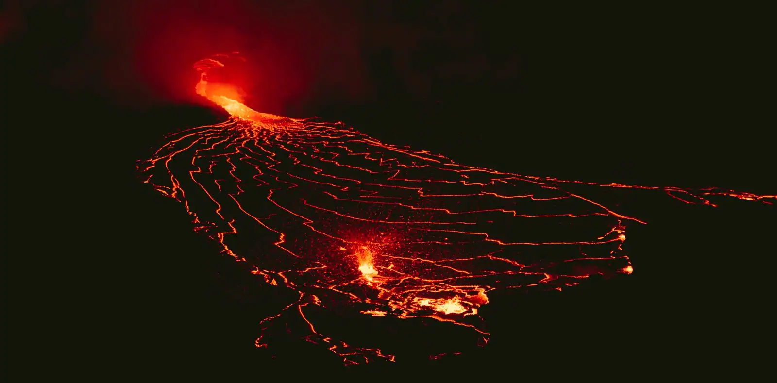 Coulée de lave incandescente s'étalant en éventail depuis une bouche éruptive, photographiée de nuit