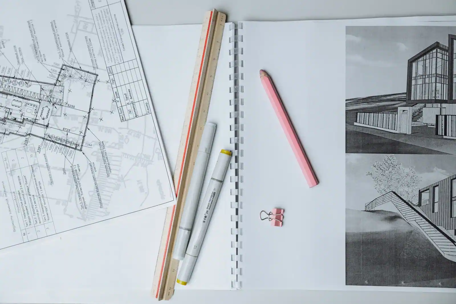 Plans d'architecte d'une maison, tirages de rendus et instruments de dessin posés sur une table.