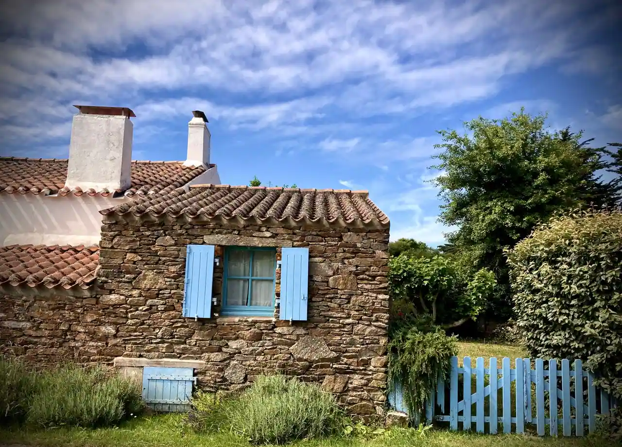 Petite maison en pierre aux volets bleus, toit de tuiles et jardin clos, typique d'un gîte rural.