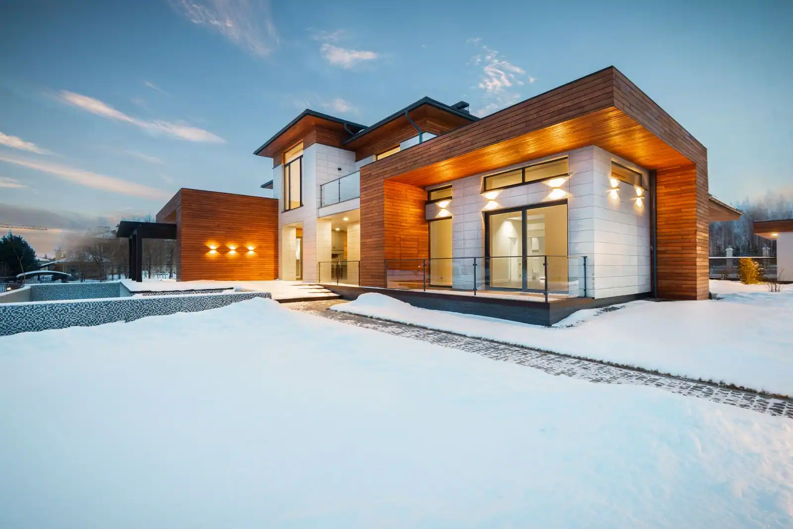 Maison individuelle neuve contemporaine, façade en bois et pierre claire, illuminée au crépuscule sous la neige.